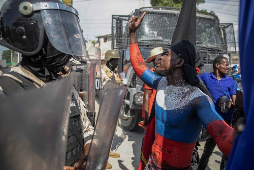 Un manifestante con los colores de la bandera nacional rusa pintada en su cuerpo discute con la policía frente a la Embajada de Estados Unidos durante una protesta para rechazar una fuerza militar internacional solicitada por el gobierno y exigir la renuncia del primer ministro Ariel Henry, en Port-au. -Prince, Haití, ayer lunes. El Consejo de Seguridad de las Naciones Unidas está evaluando la solicitud del gobierno haitiano para el despliegue inmediato de tropas extranjeras para ayudar a liberar a Haití de las garras de las pandillas que han causado escasez de combustible, agua y otros suministros básicos. (Foto AP/Odelyn Joseph)