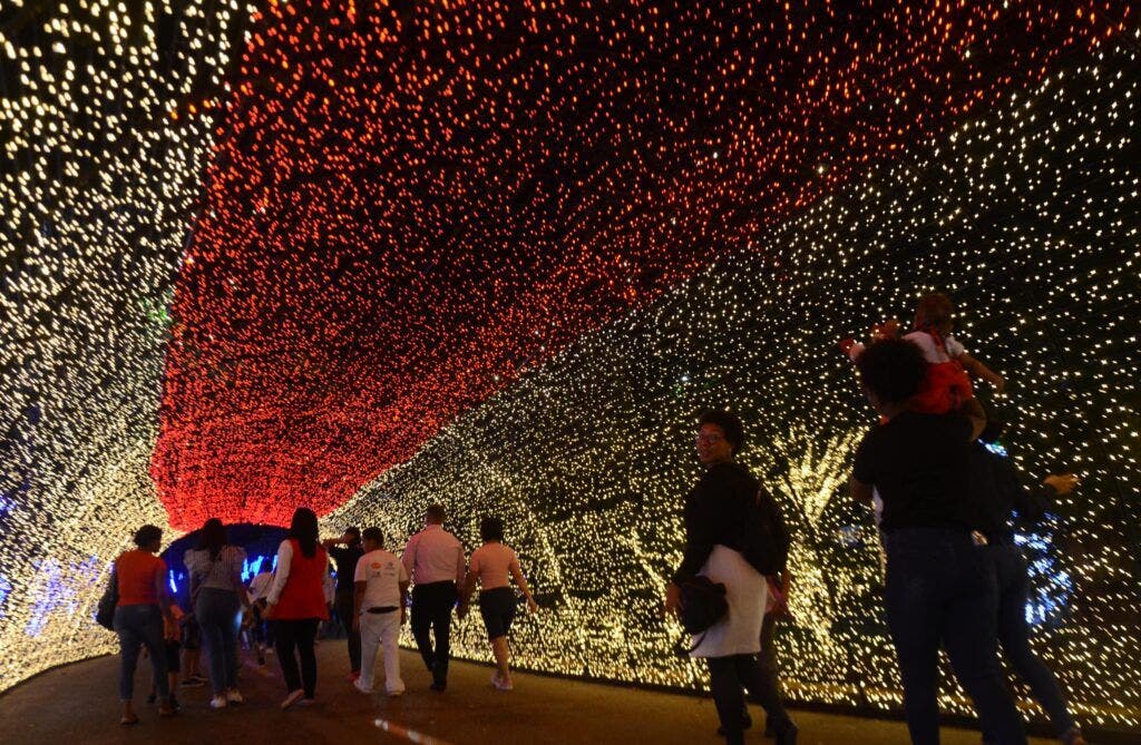 Un grupo de personas camina por el túnel de luces multicolores, uno de los escenarios de Villa Navidad 2023, un espacio de recreación para toda la familia, decorado con miles de luces y en el cual personajes como Santa Claus y los Reyes Magos llevan alegría e interactúan con quienes visitan el lugar, abierto hasta el 7 de enero, en el Centro Olímpico Juan Pablo Duarte, en la capital