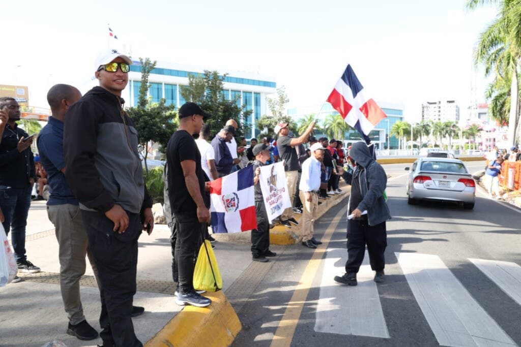 Grupo de personas agitan banderas en la avenida 27 de Febrero previo a tomar los autobuses para participan en la marcha pacífica en El Hoyo de Friusa