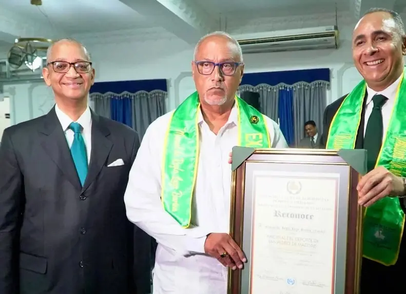 Manuel de Regla Lugo, en representación de Manuel ‘Varilla’ Lugo, recibe la placa de su fallecido padre de manos de Nelson Arroyo.  Le acompaña el edecán, periodista Osvaldo Rodríguez Suncar.