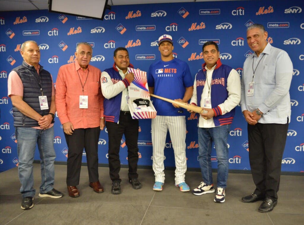 Juan Soto, superestrella de los Mets de Nueva York (centro) recibe un bate con la proclama de Embajador de los XXV Juegos Centroamericanos y del Caribe Santo Domingo 2026, que le entregan José P. Monegro, presidente del Comité Organizador,  y el ministro de Deportes Kelvin Cruz. Le acompañan, desde la izquierda, Garibaldy Batista, Luisín Mejía y, en el extremo derecho,  el cónsul dominicano en Nueva York, Jesús- Chu-Vásquez.