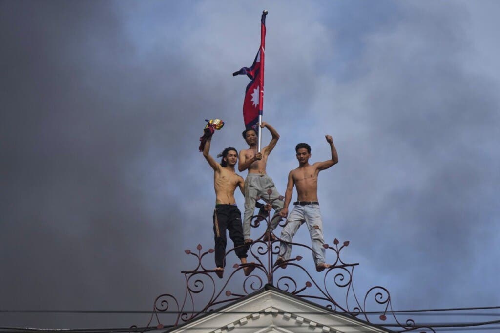 Manifestantes celebran desde la cima del Singha Durbar, la sede de varias agencias y oficinas del gobierno, después de prenderle fuego al edificio durante una protesta contra las restricciones a redes sociales y la corrupción, el martes 9 de septiembre de 2025, en Katmandú, Nepal. (AP Foto/Niranjan Shrestha)