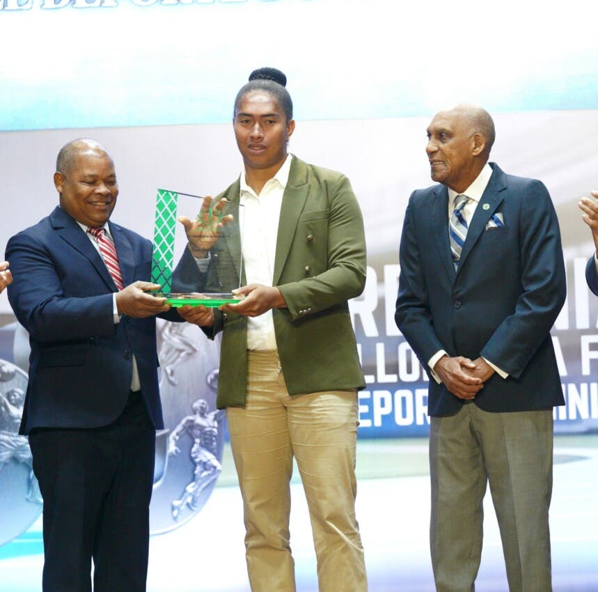 Yudelina Mejía, junto a William Ozuna, muestra la placa de reconocimiento entregada por miembros del comité permanente del Pabellón de la Fama. Figura en la imágen Juan Niemen.