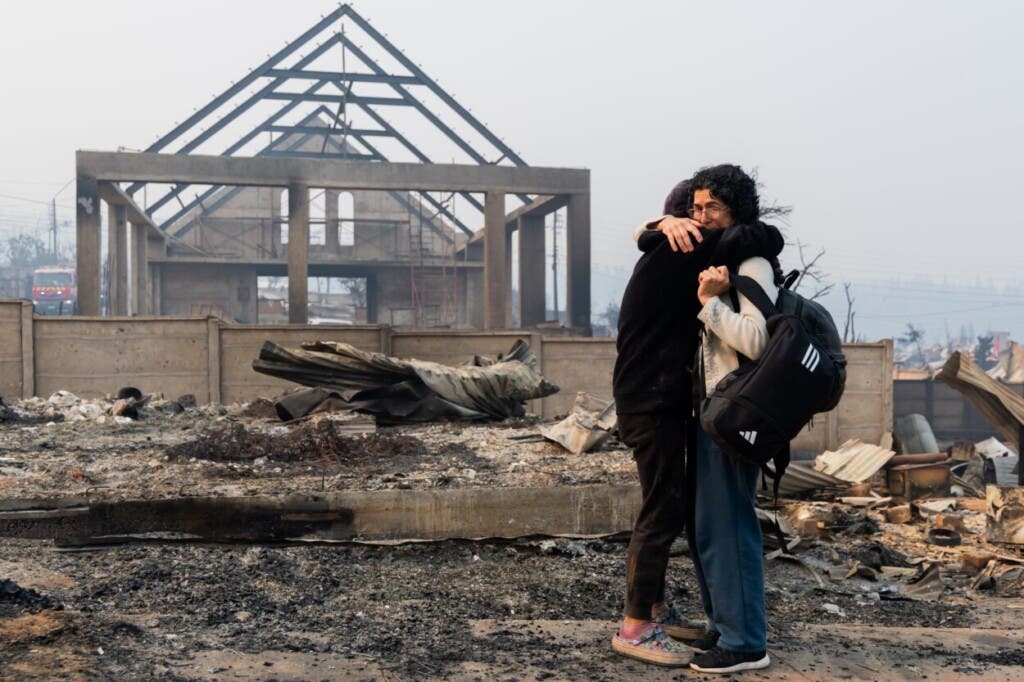 Mirtza Aguilera, a la derecha, y su hija se abrazan frente a su casa quemada por los incendios forestales en Tomé, Chile, el lunes 19 de enero de 2026. (AP Foto/Javier Torres)